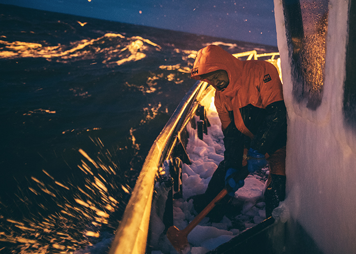 A fisherman uses a big hammer to break up ice on the deck.